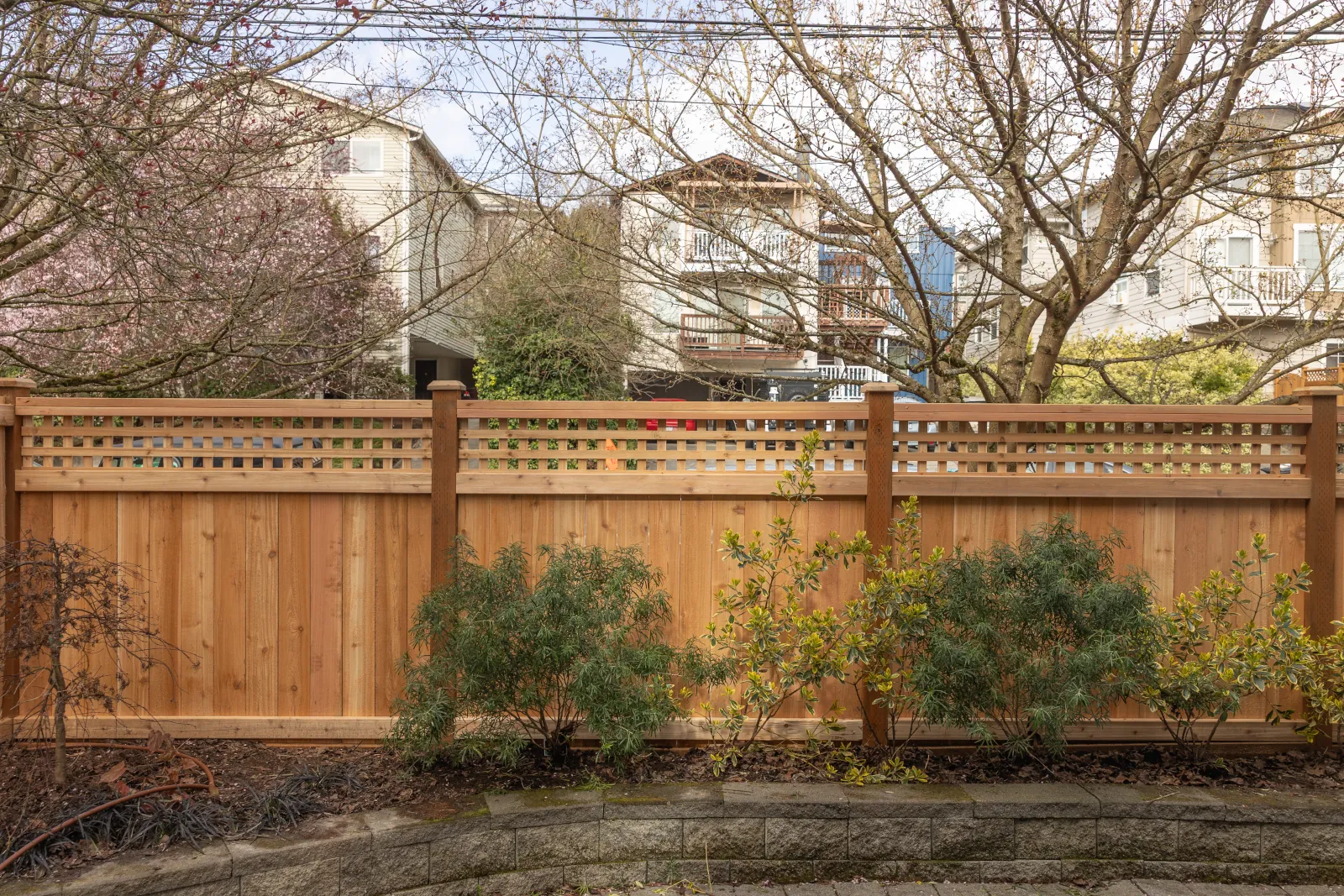 New cedar fence with square lattice top above a block retaining wall and shrubs