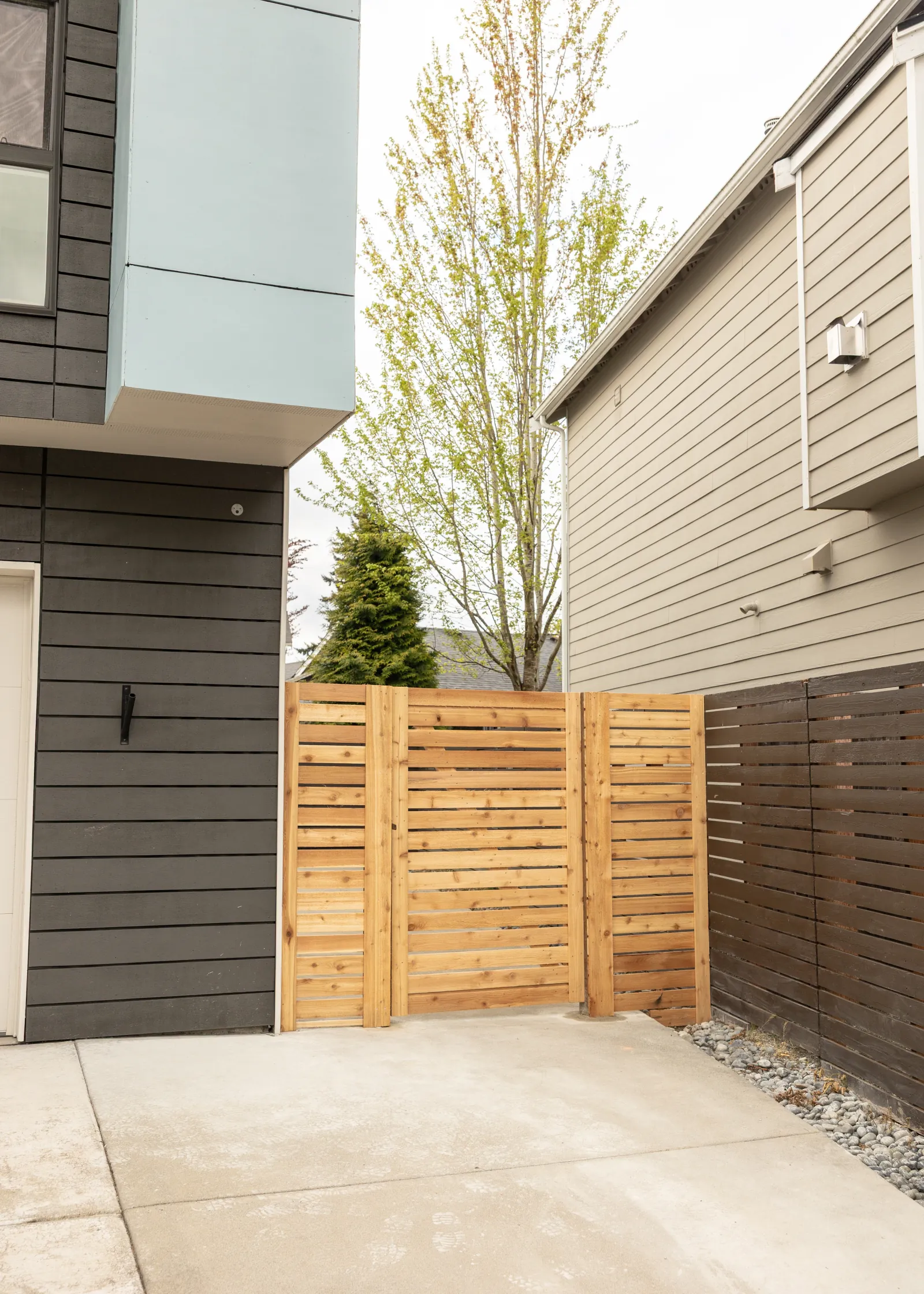 New horizontal slat cedar fence and gate enclosing a side yard, joined to an existing dark-stained horizontal fence