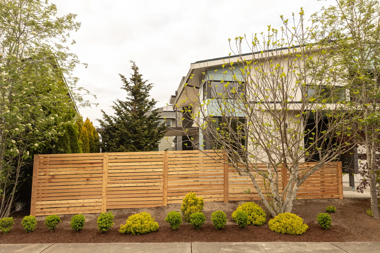 Horizontal cedar slat fence with staggered panels screening a modern home