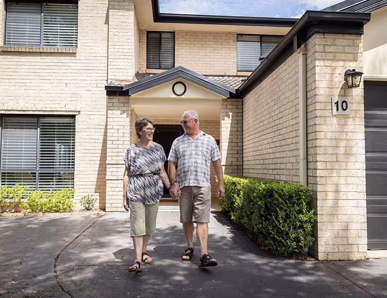 Old couple holding hands in front of house
