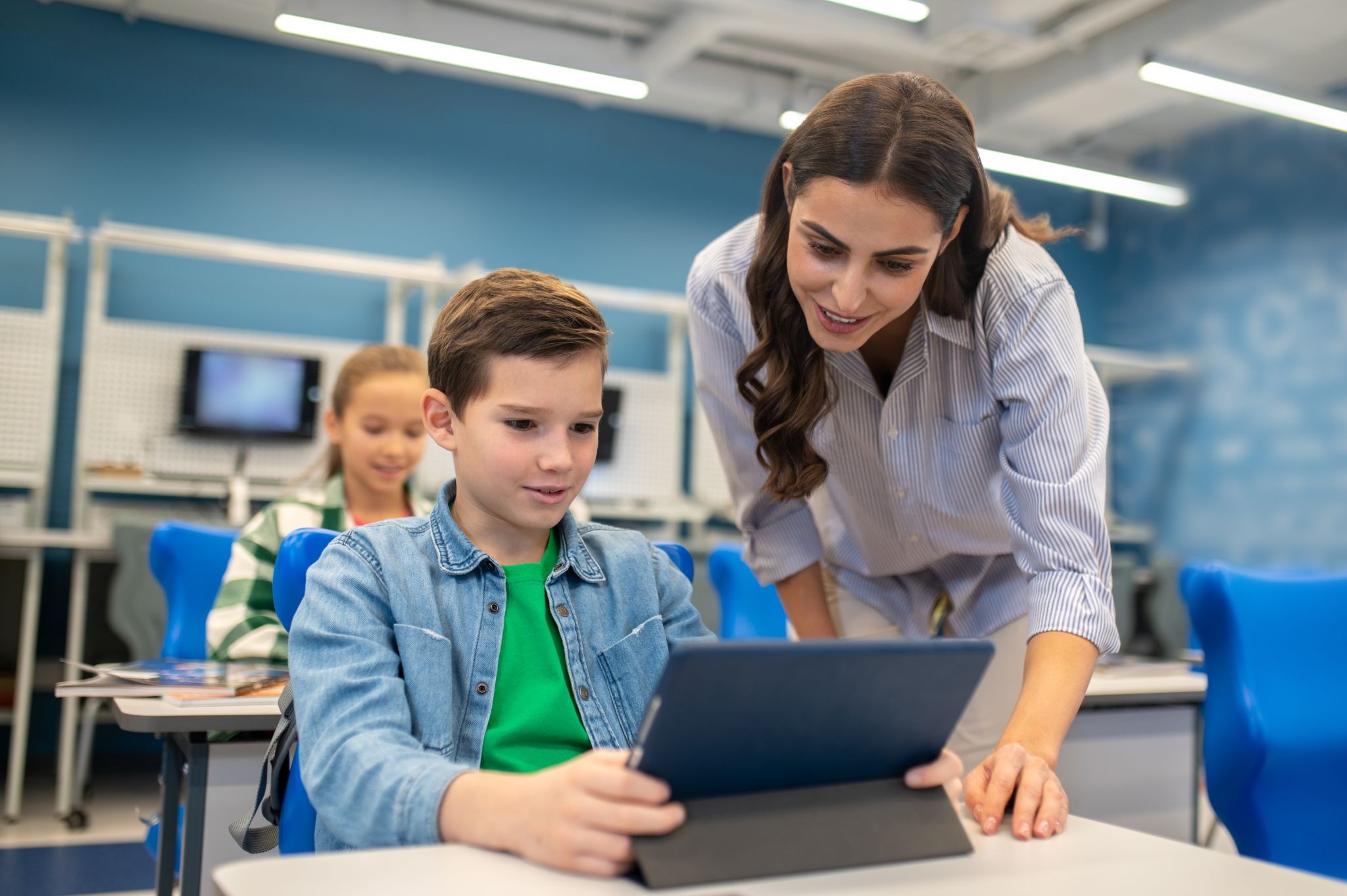 A teacher helping student with a tablet sitting in a digital classroom showcasing personalized learning.