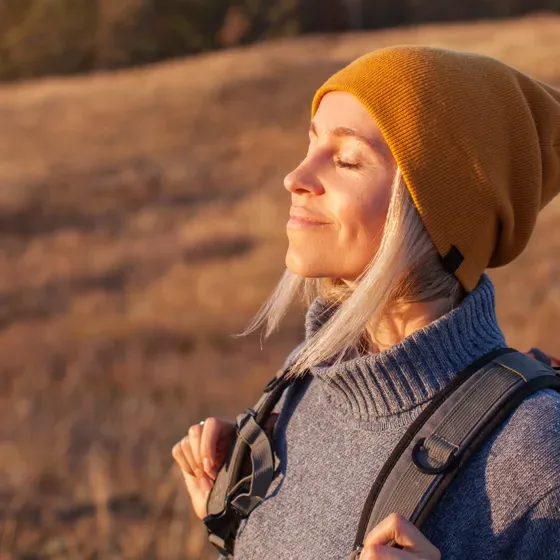 A woman in a beanie smiling with her eyes closed in low sun