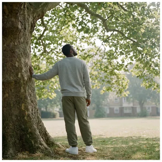A man resting a hand on a large tree trunk in a park