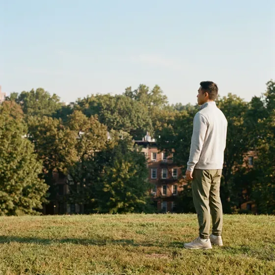 A man standing on a hilltop lawn looking out