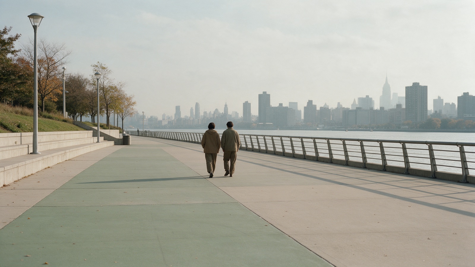 Two people walking side by side along a river promenade, seen from behind at a distance