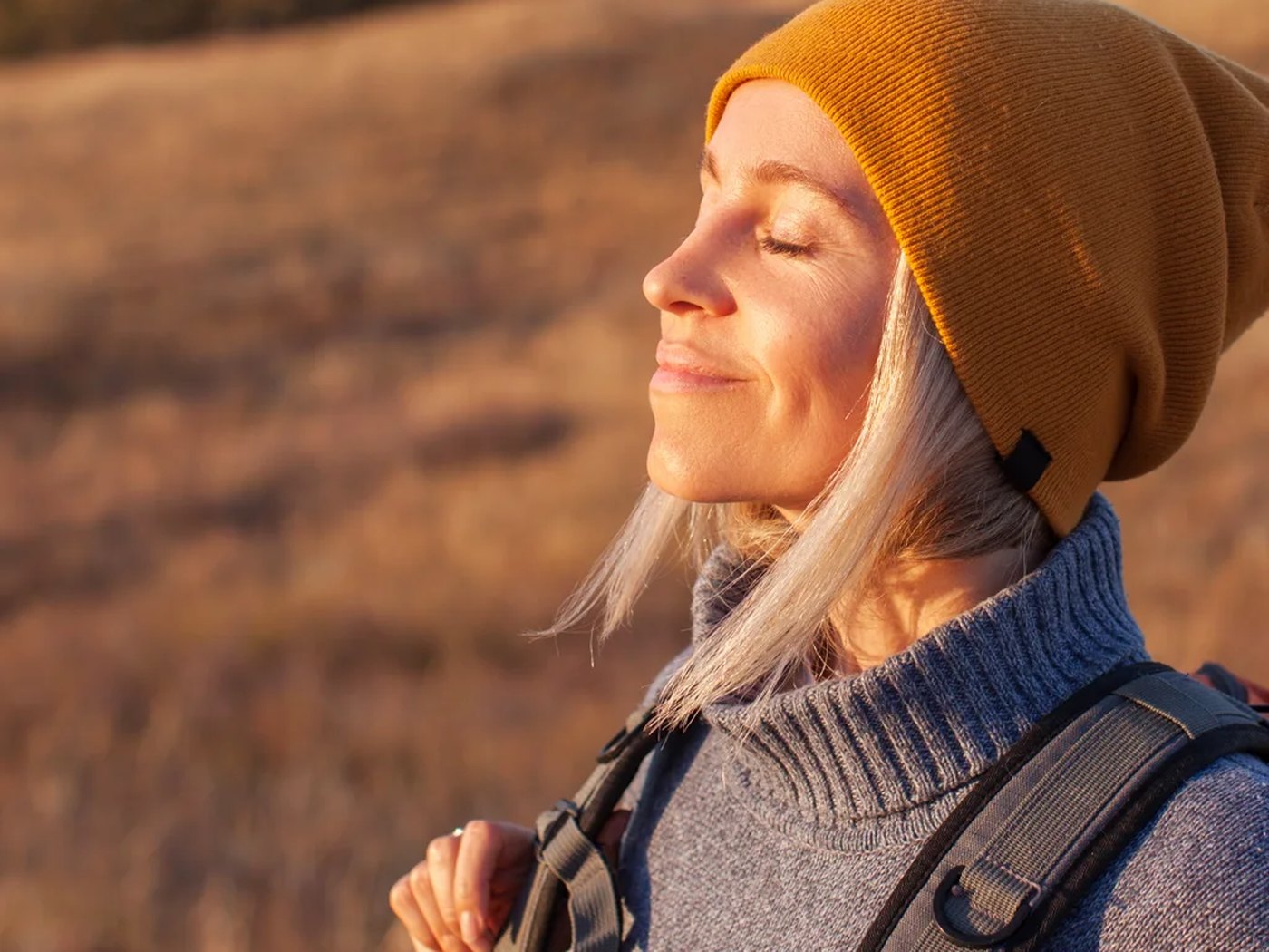 A woman in a beanie with her eyes closed in low winter sun