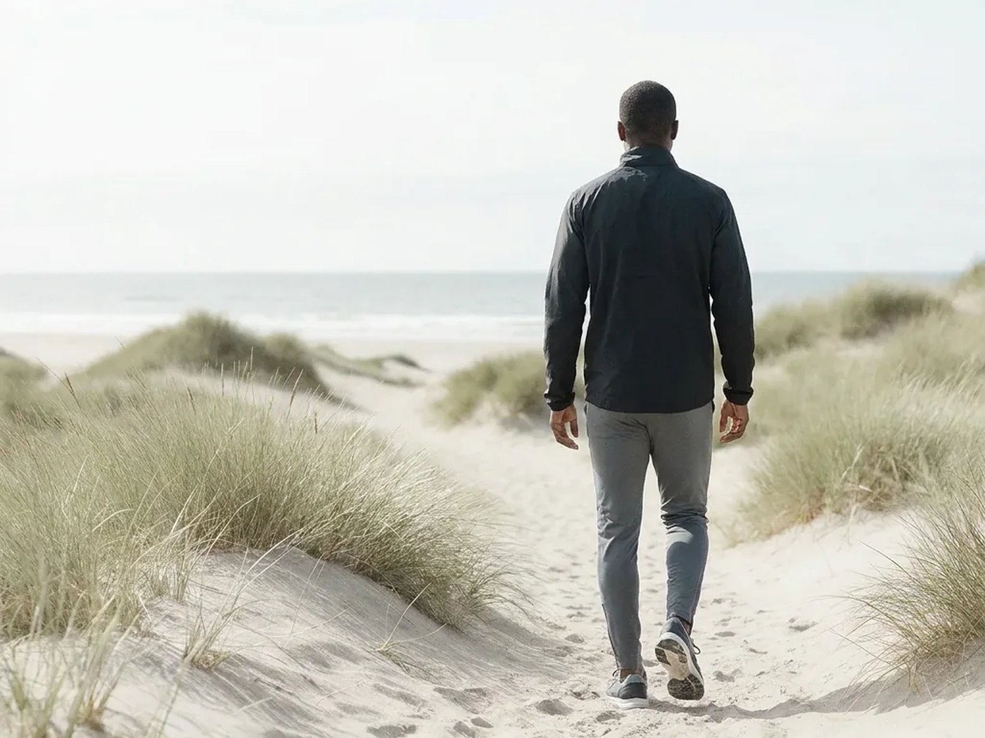 A man walking alone along a dune path toward the beach
