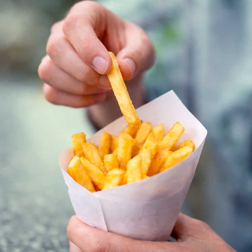 Hand die een frietje uit een puntzak Belgische frieten neemt