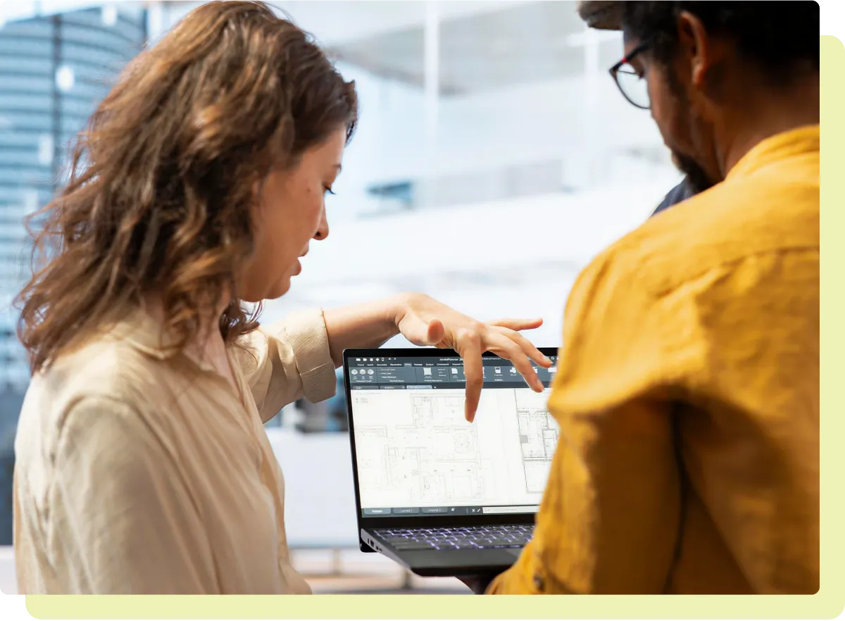 Two people reviewing architectural plans on a laptop in a modern office.