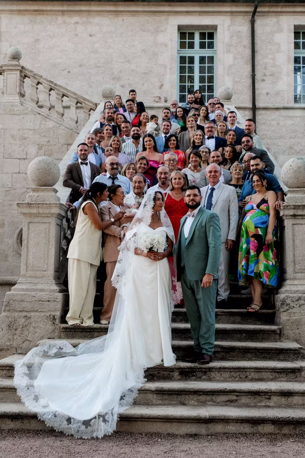 Mariés entourés de leurs proches sur l’escalier du Domaine de la Chartrognière, souvenir convivial du mariage