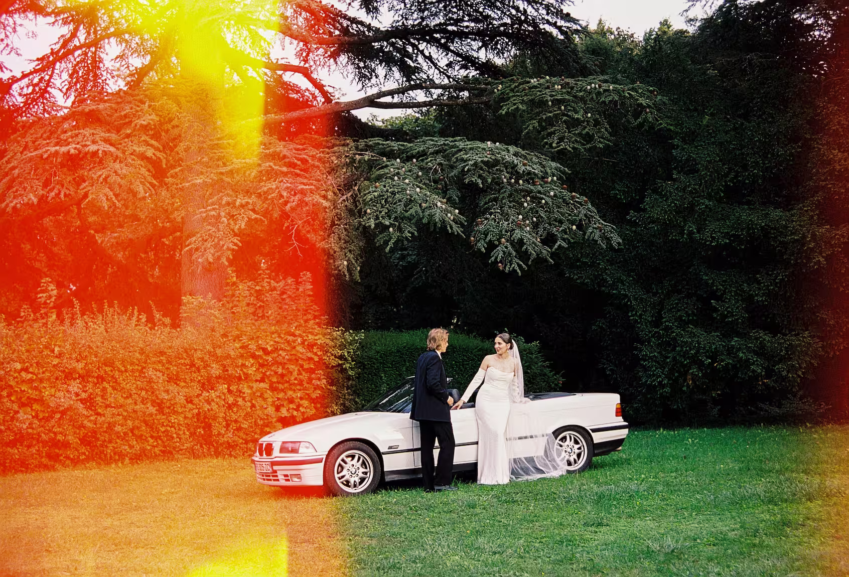 Mariés près d’une voiture décapotable au Domaine de Tourieux, photographiés en argentique avec une fuite de lumière.