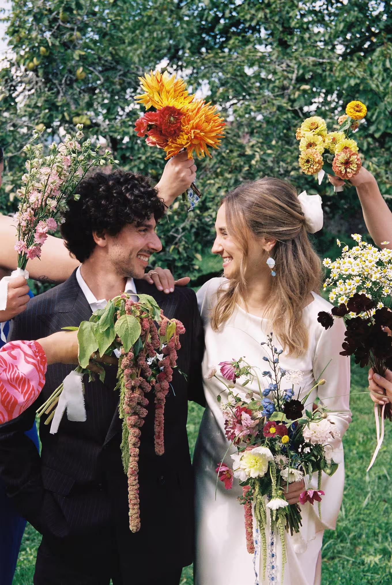 Mariés souriants entourés de bouquets colorés lors d’une cérémonie en plein air à la Ferme de Gy.