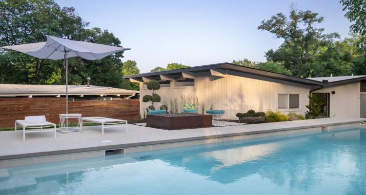Backyard pool with lounge chairs and a white umbrella in front of a low mid-century house
