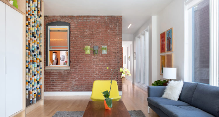 Living space with an exposed brick wall, colorful artwork, a yellow armchair and a blue sofa