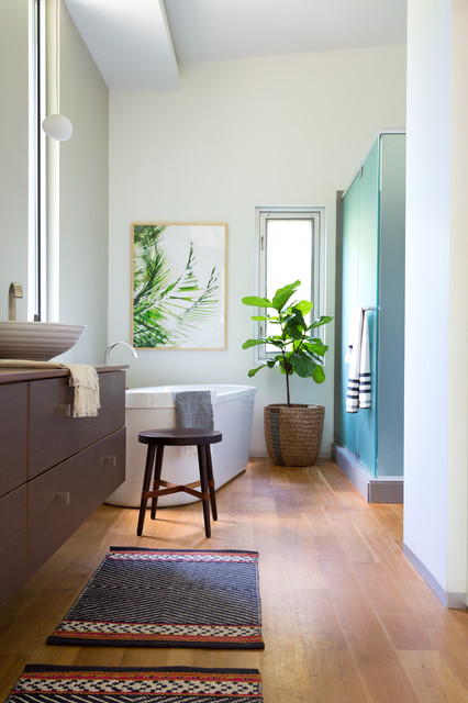 Contemporary bathroom with a freestanding white tub, a wood vanity with a vessel sink, a teal glass shower enclosure and a patterned runner on a wood floor