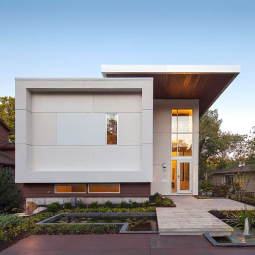 Modern house exterior with white stucco volumes and a warm wood soffit over the entry, with a planted walk to the front door