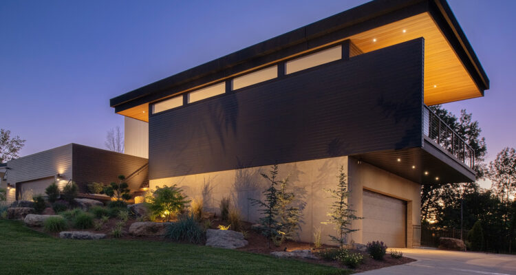 Modern house at dusk with an angled roofline and glass walls lit from within