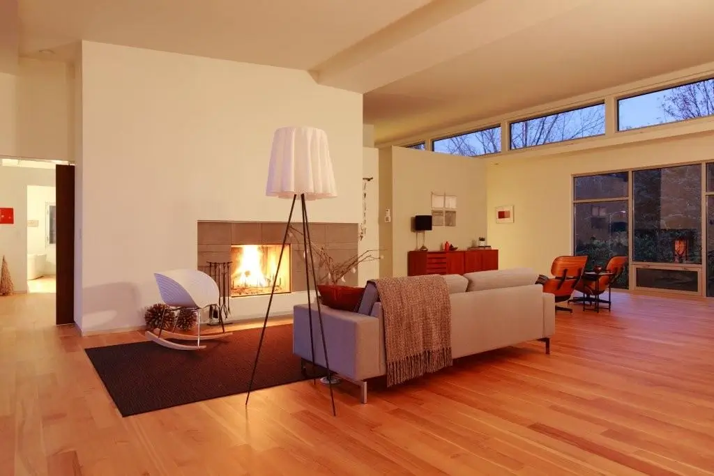 Open living room at dusk with a tiled fireplace, a gray sofa, a tripod floor lamp and a band of clerestory windows