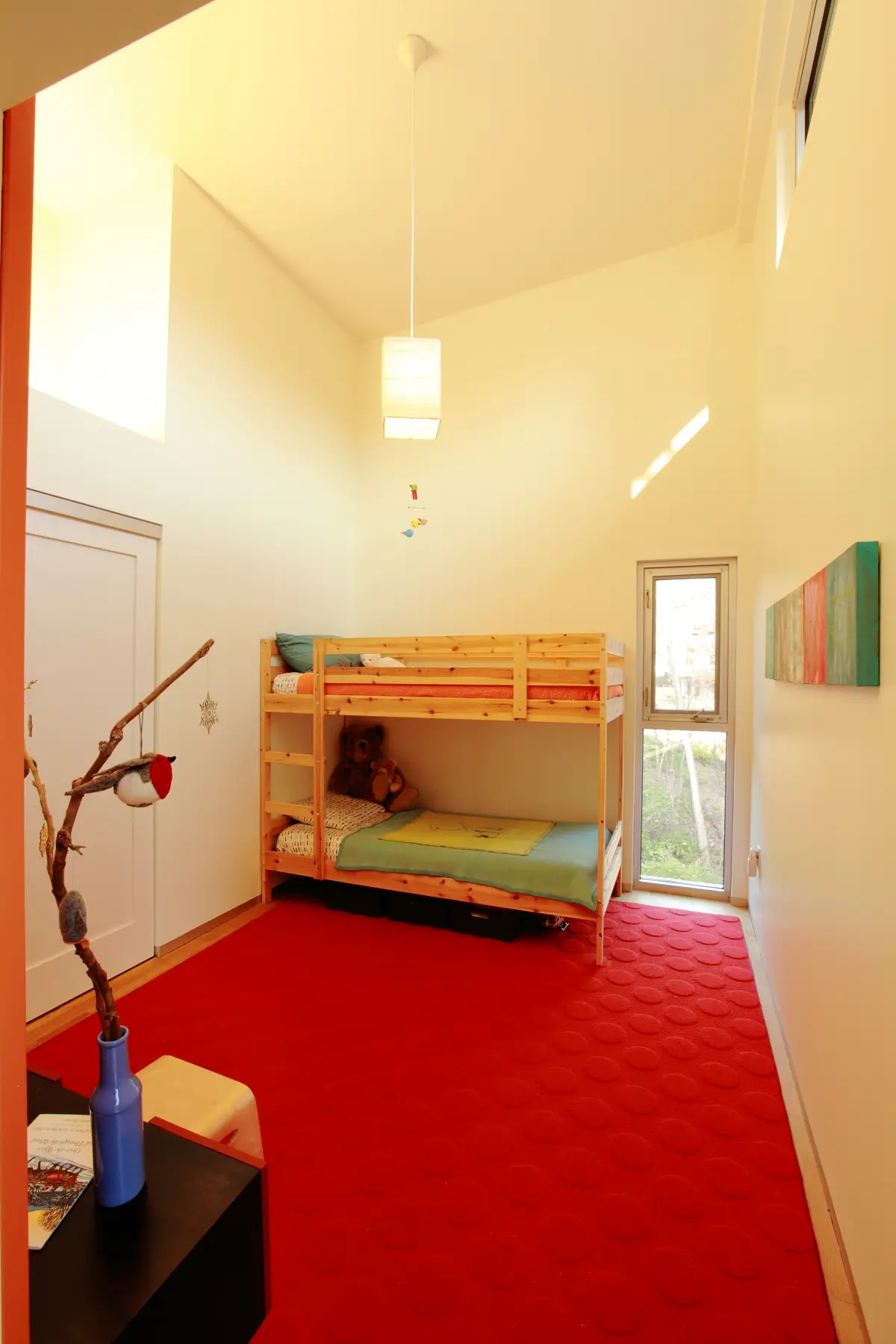 Child’s bedroom under a tall sloped ceiling, with a wooden bunk bed, a red rug and a narrow glass door to the outside
