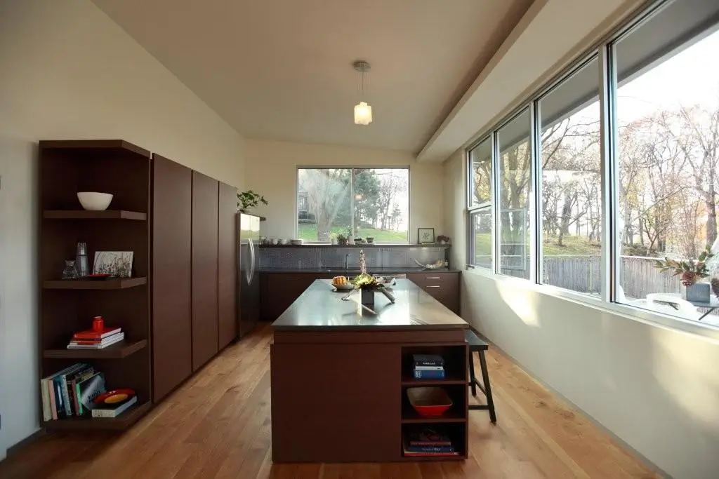 Galley kitchen with dark wood cabinetry, a long island and a band of windows looking out to the trees