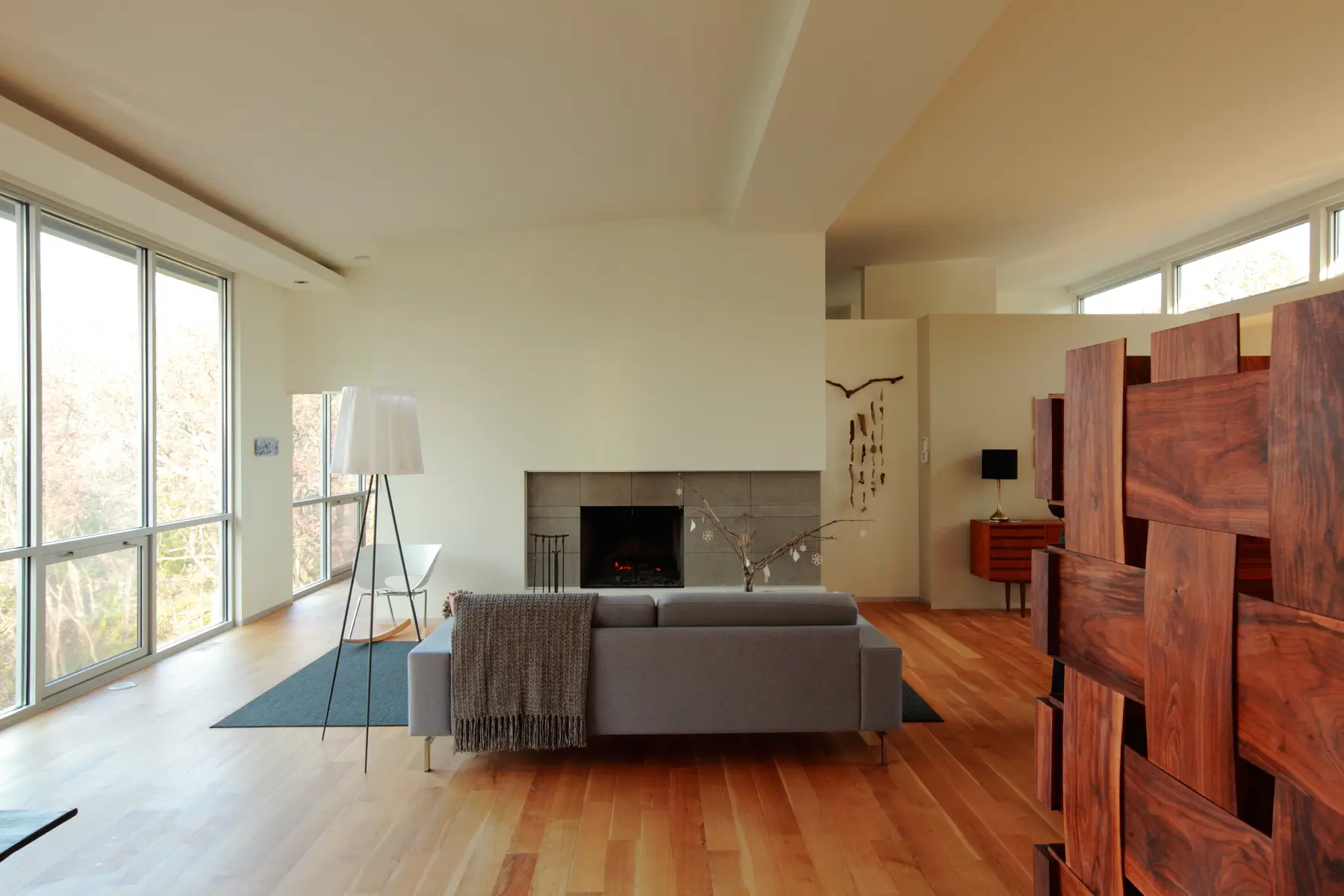 Living room with floor-to-ceiling glass on one side, a gray sofa facing the fireplace, and a woven wood screen wall in the foreground