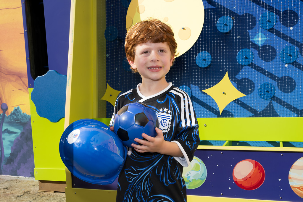 little boy smiling while holding a soccer ball at the Planet Soccer Exhibit in the Miami Children's Museum