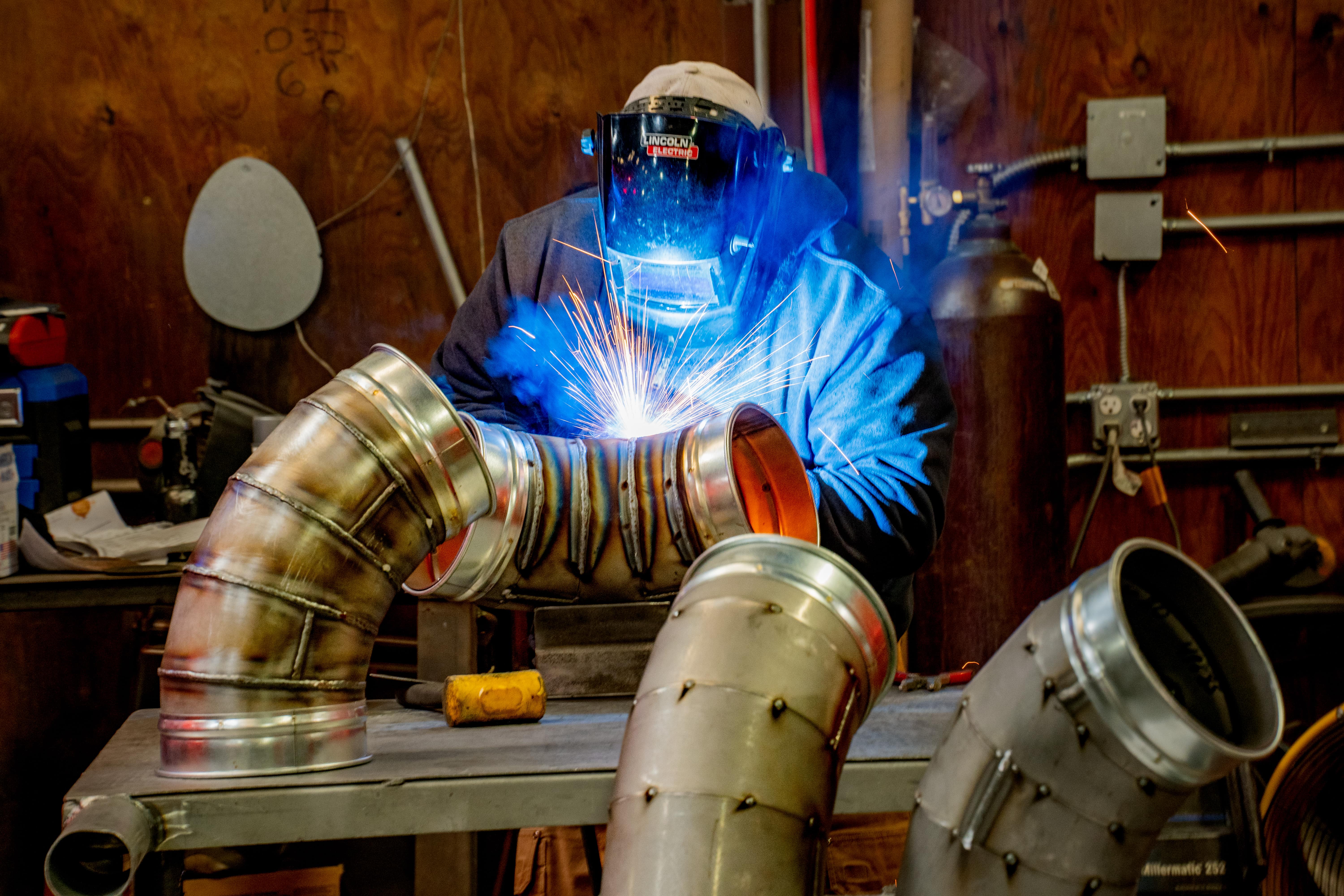 A welder fabricating segmented duct elbows.