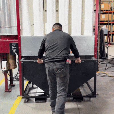 Man quickly swaps a gray hopper container on industrial equipment in a warehouse.