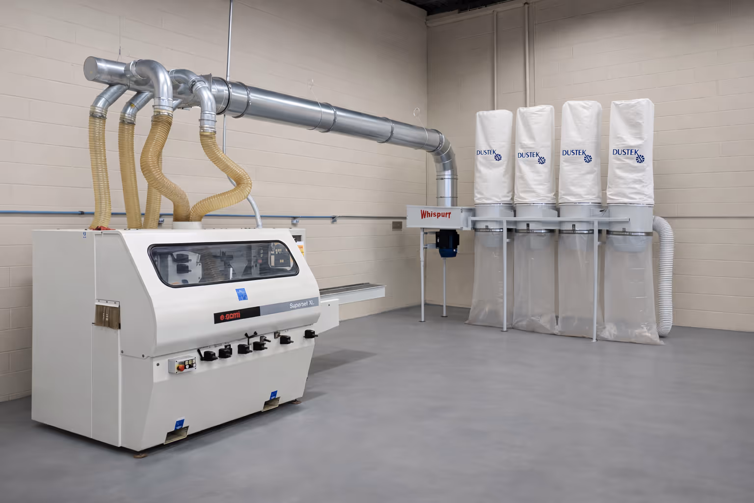 Industrial woodworking machine connected to a Dustek dust collection system with four white filter bags in a clean workshop.