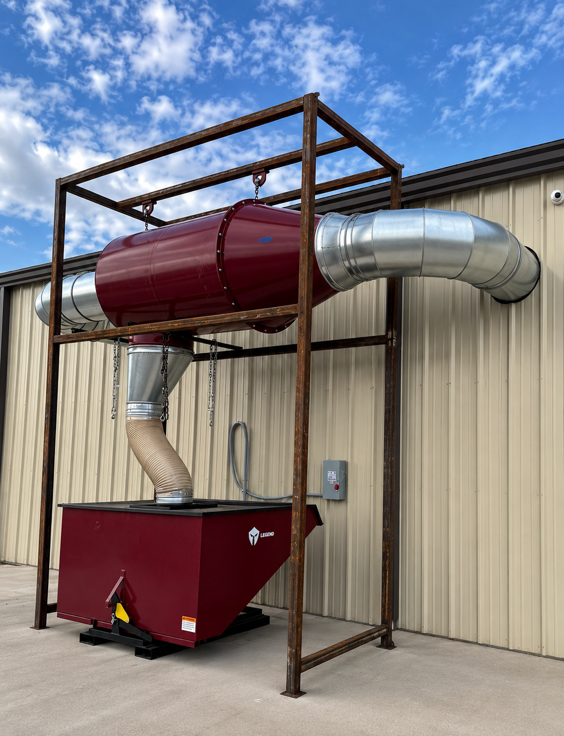 Industrial red duct system attached to a beige metal building with blue sky and clouds above.