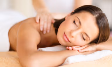 Relaxed woman with closed eyes lying face down on a massage table receiving a shoulder massage.