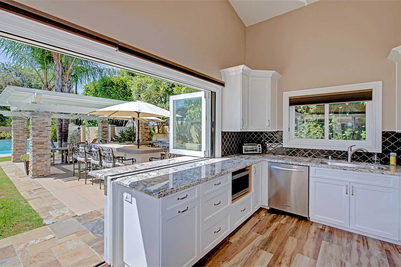 Pool house with bifold window and bifold door meeting at center, creating a fully open-air space. White painted interior, pool visible in background.