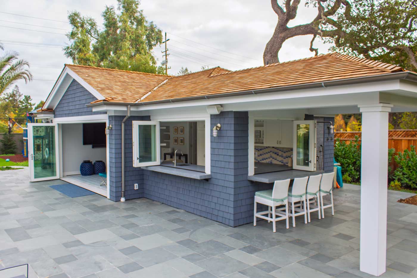 Backyard pool house with two 3-panel bifold passthrough windows, each with an exterior bar counter. Pool in foreground, 4-panel bifold door between the windows.