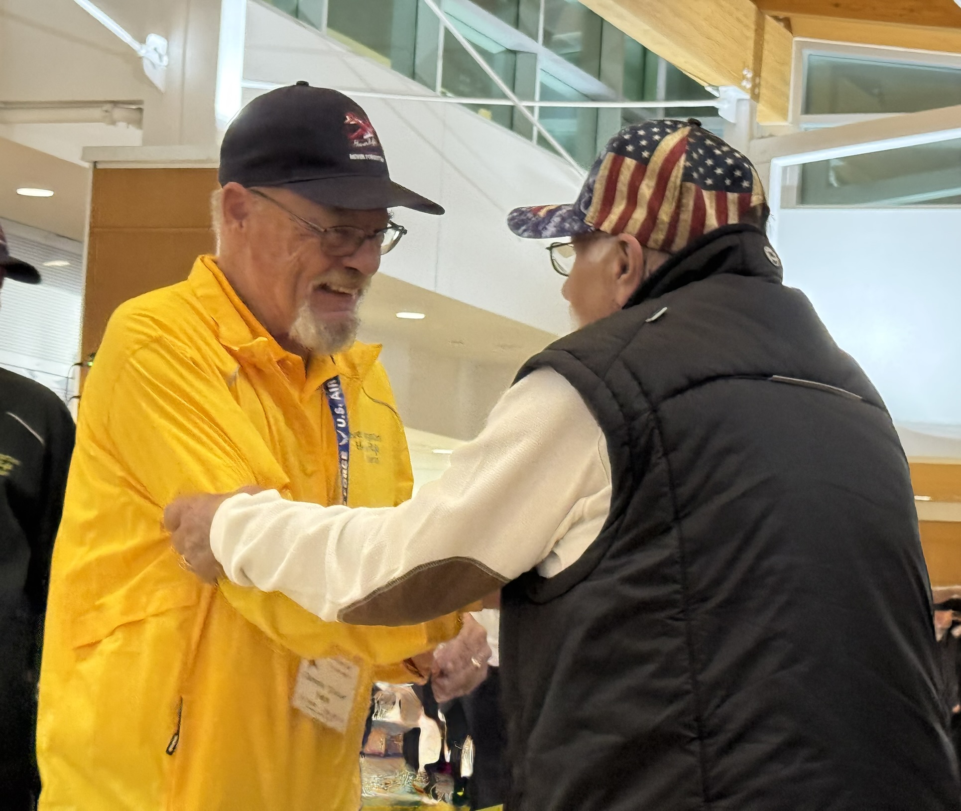 Image of two veterans in hats greeting each other at the airport.