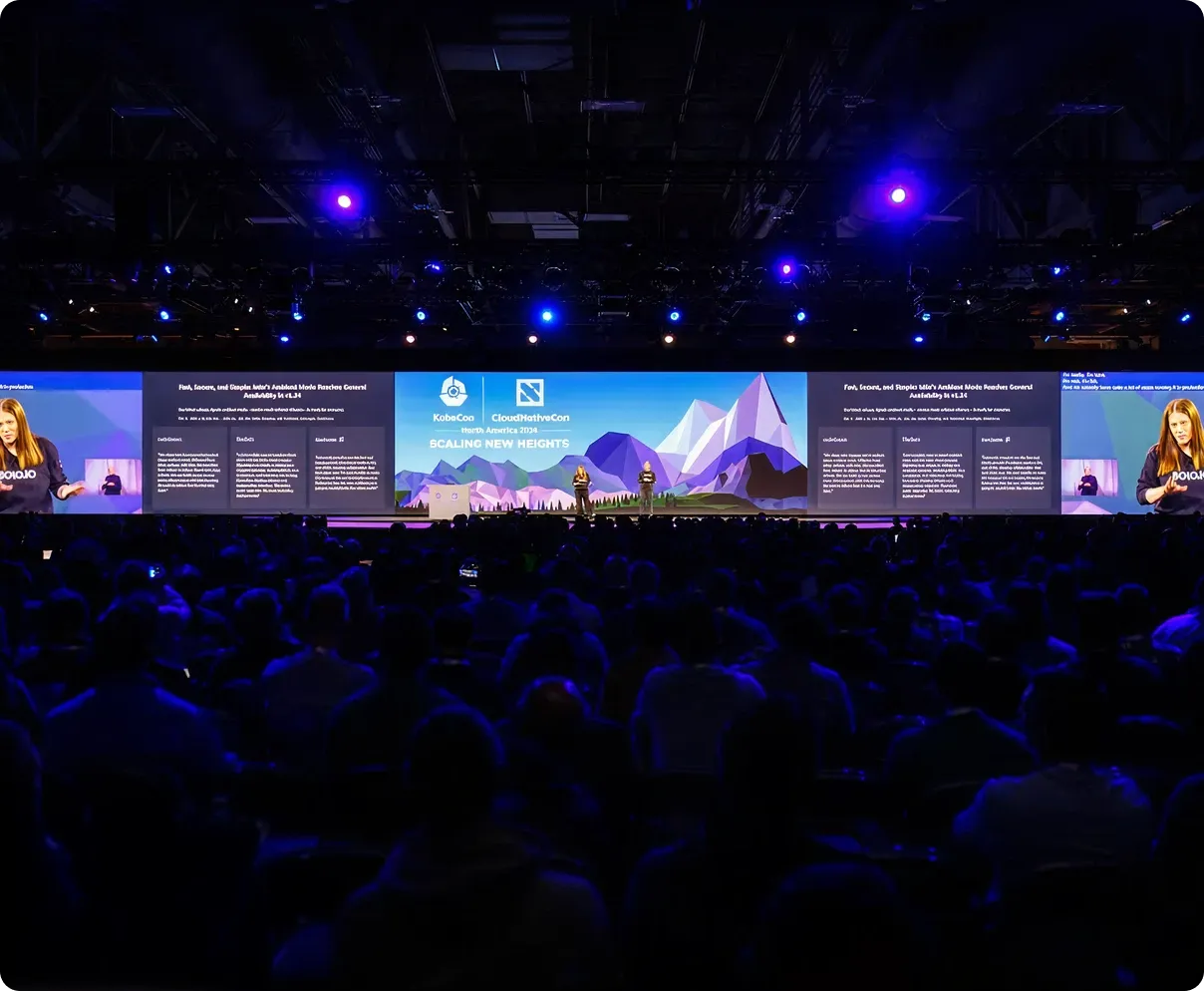 Large audience watching two presenters on stage with a wide screen showing 'KubeCon + CloudNativeCon North America 2019 Scaling New Heights' and presentation slides.