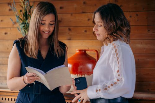 Twee vrouwen in gesprek tijdens een coachingsessie, kijkend naar een notitieboek in een warme, natuurlijke setting – onderdeel van het FLOW-traject bij Oraflow.