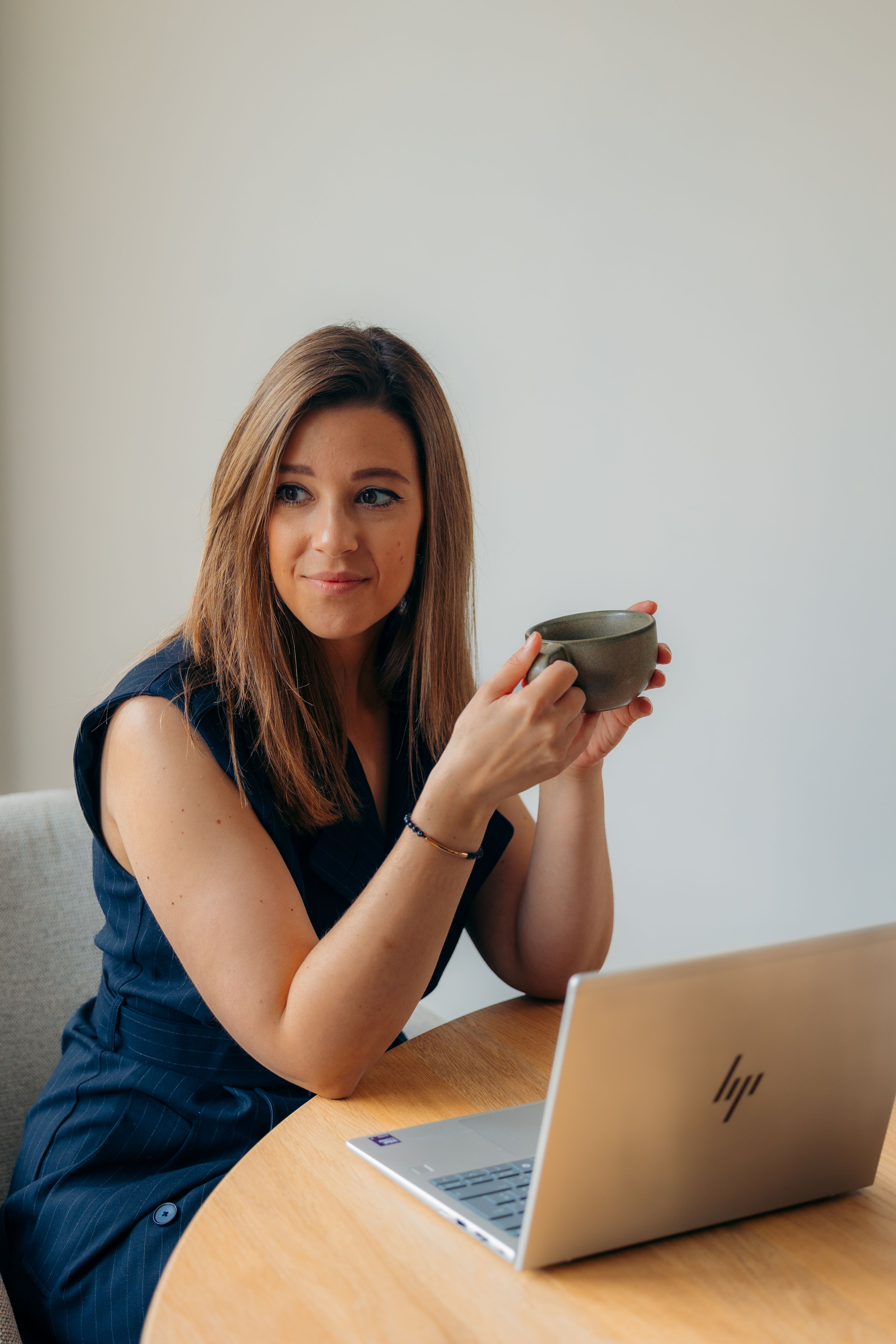 Laura Gielis zit in een zakelijke setting ontspannen met een kop koffie in de hand – uitnodiging tot persoonlijk contact en begeleiding op maat voor bedrijven.