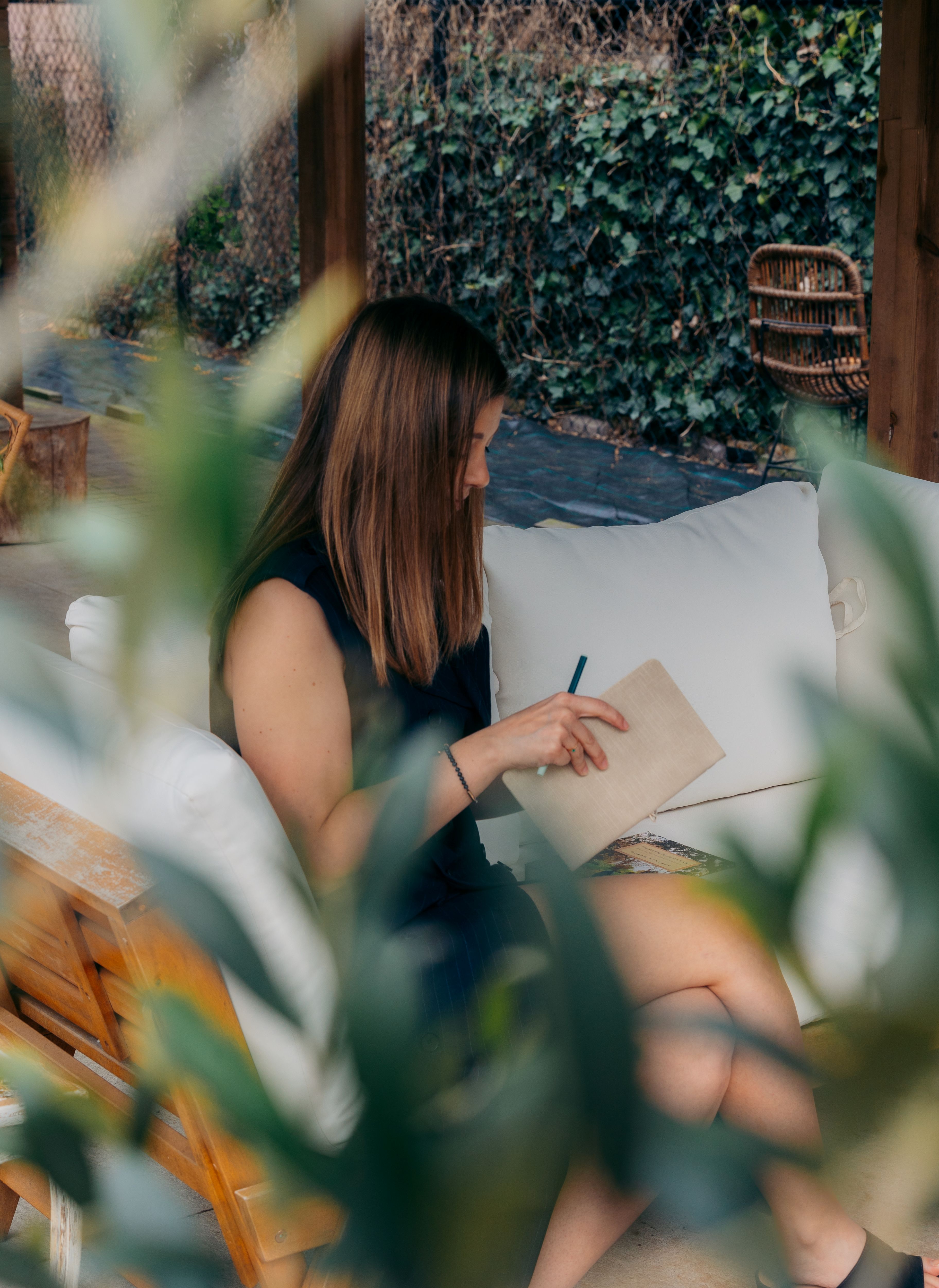 Vrouw schrijft in een notitieboek in een tuinsetting – reflectie over authentiek ondernemen en het loslaten van het imposter syndrome.