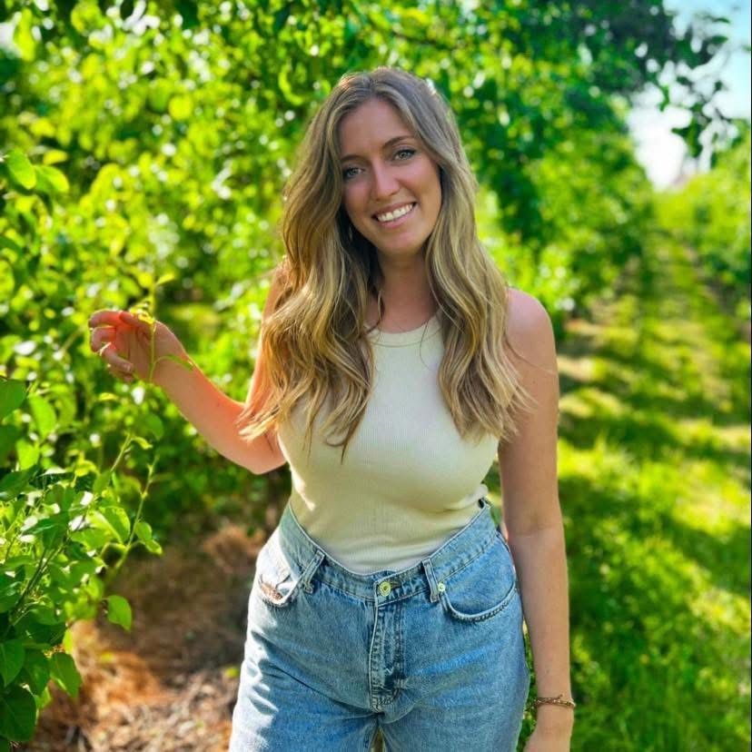 Ilona, begeleidster pleegzorg, glimlacht ontspannen terwijl ze in een boomgaard staat, klanttestimoniaal over kerntalentenanalyse bij Laura Gielis.