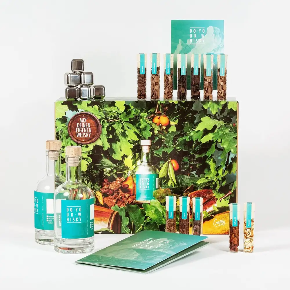 DIY-Whisky-Set mit Holzchips und Botanicals in Reagenzgläsern, zwei Flaschen und Whiskysteinen aus Edelstahl in einer Geschenkbox.