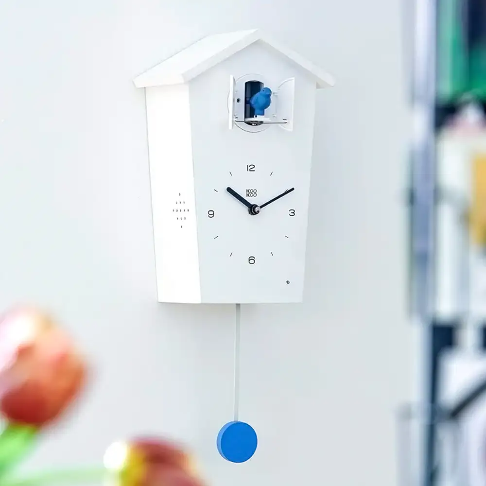 KOOKOO BirdHouse Kuckucksuhr in Weiß mit Pendel und kleinem farbigem Vogel am geöffneten Türchen, modernes Design an einer Wand.