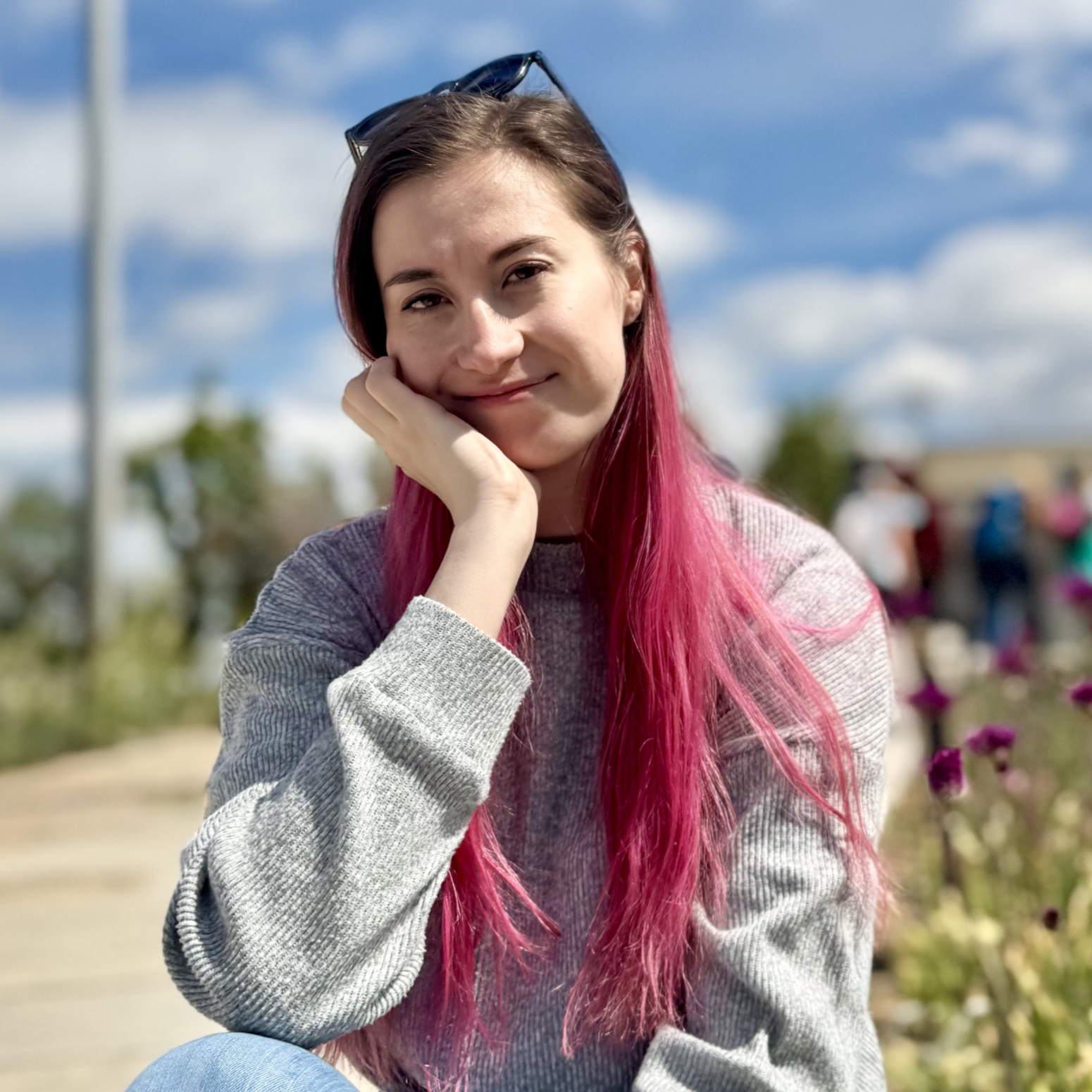 Photo of Linde Botes with long pink hair resting her head on her hand outdoors on a sunny day.