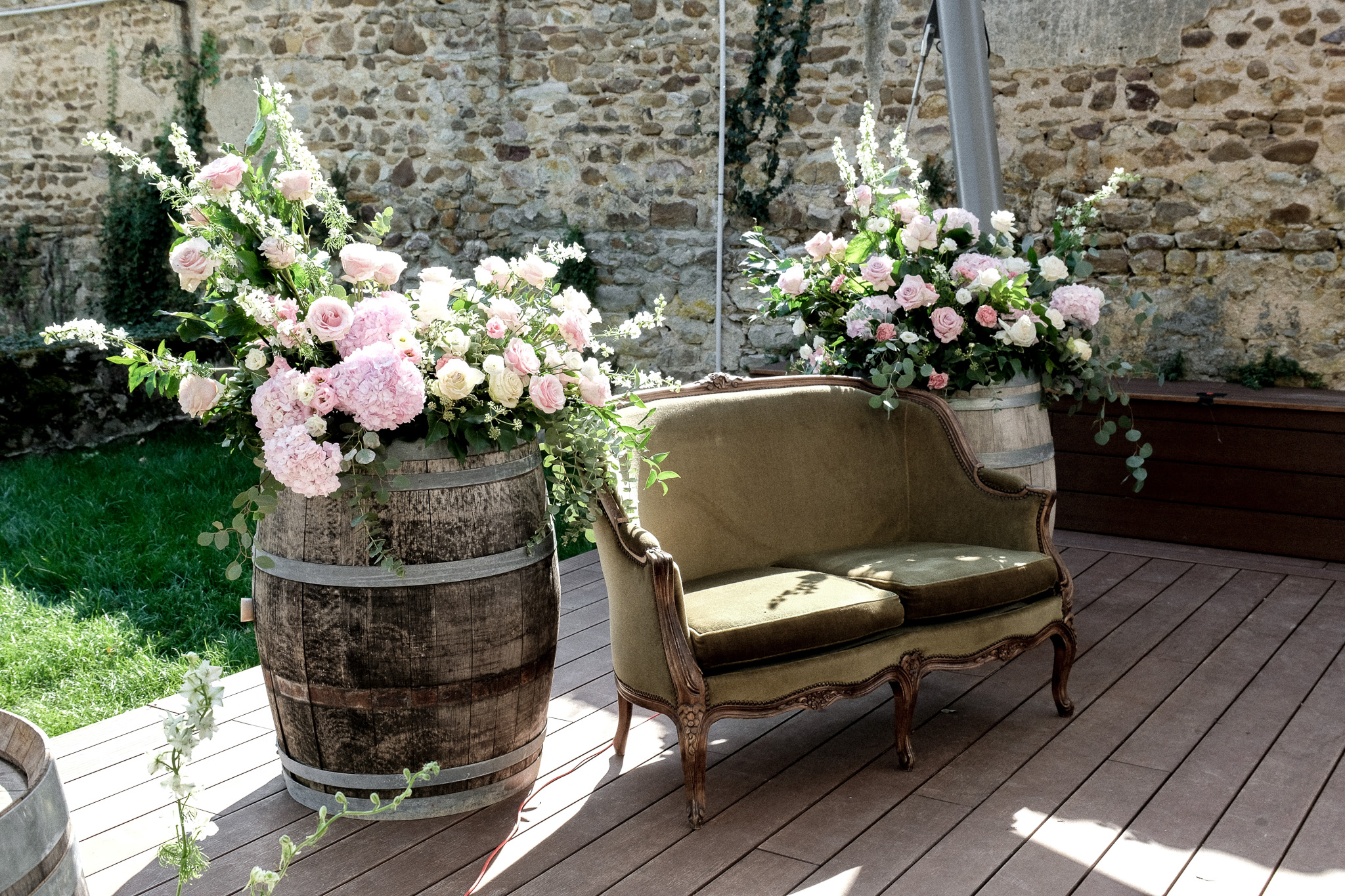 Tonneaux fleuris de roses et hortensias autour d’un canapé vintage pour une décoration de mariage.