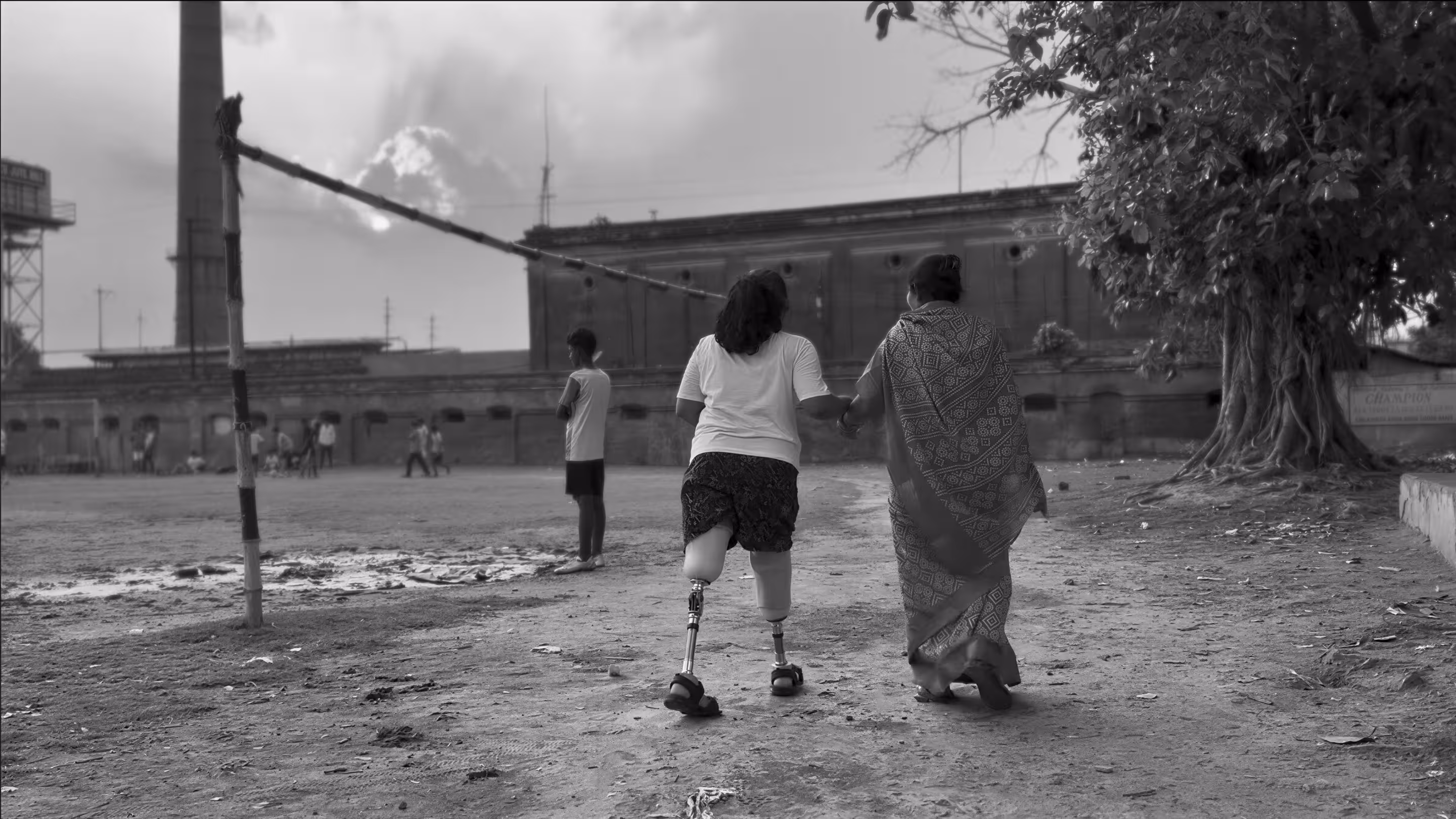 A mother walking with her amputee daughter in a playground, holding hands.