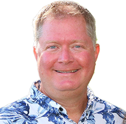 Smiling man with short blond hair wearing a blue and white floral shirt standing outdoors with green foliage in the background.