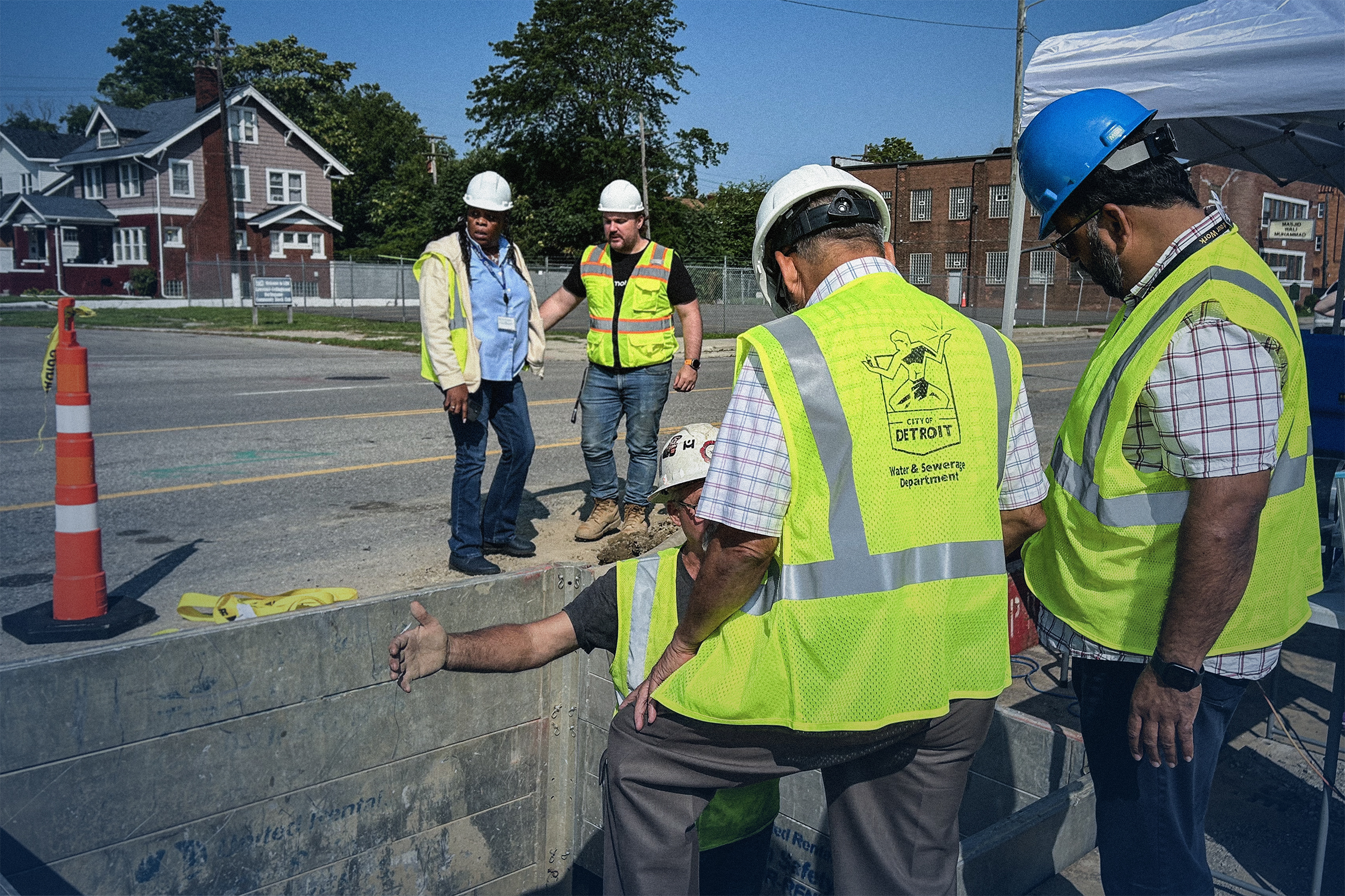 Construction workers in yellow safety vests and helmets working and communicating at an outdoor urban worksite.
