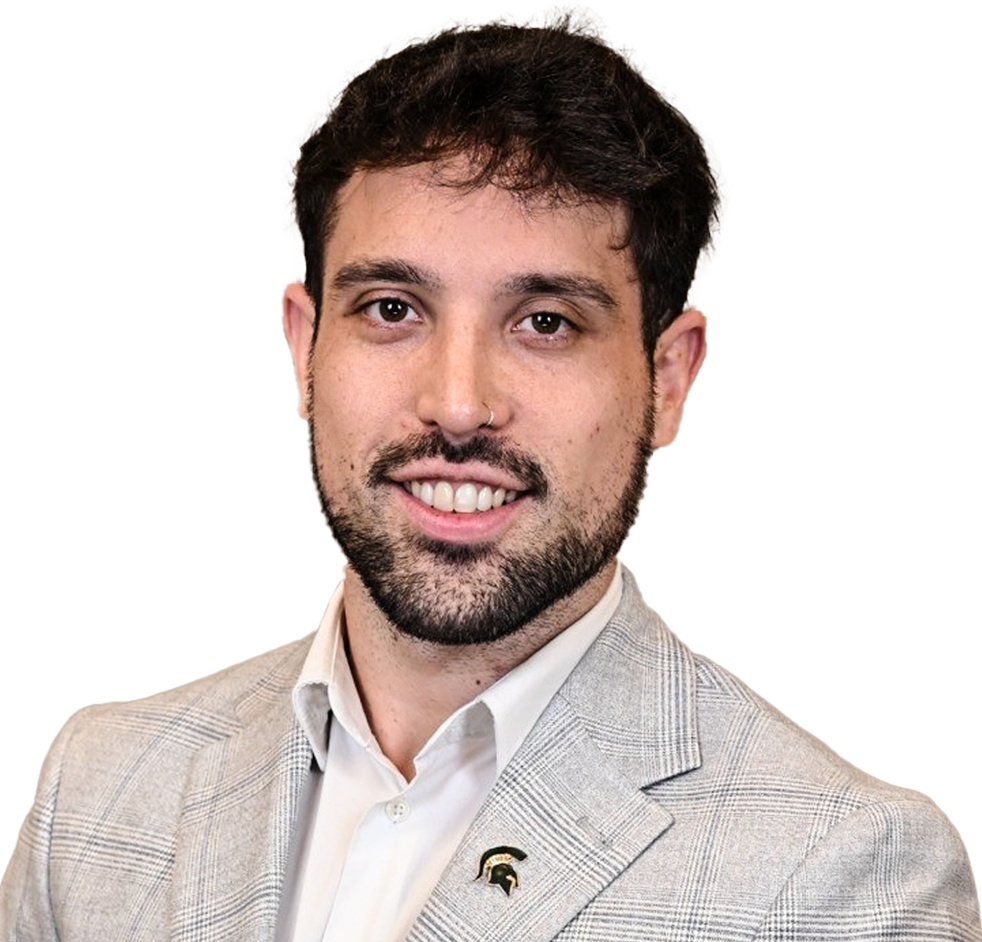 Man with dark hair and beard wearing a light gray plaid suit jacket and white shirt, smiling against a neutral background.
