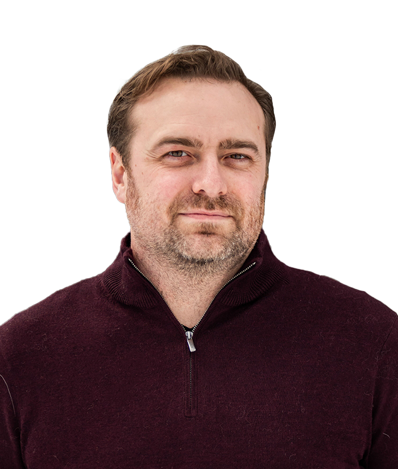 Portrait of a man with short brown hair and stubble wearing a dark maroon zip-up sweater, standing outdoors with snow-covered trees in the background.