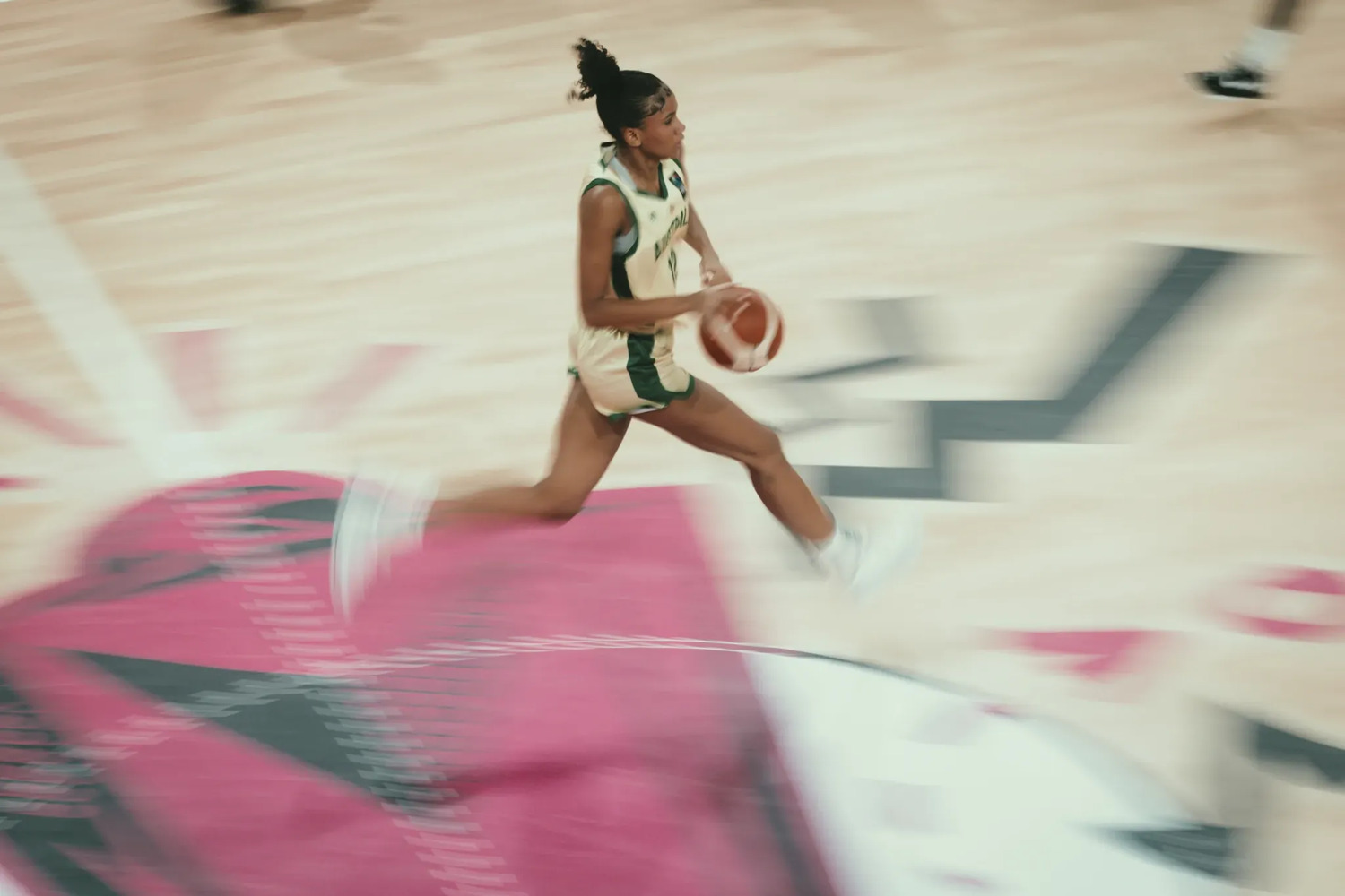 A panned motion-blur frame of Sitaya Fagan in a pale Australia uniform running the floor with the ball in her right hand, the pink and white court streaking past her.