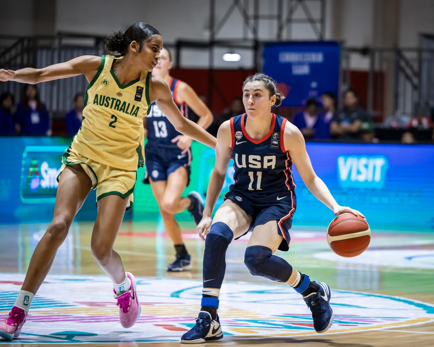 Sitaya Fagan in a gold Australia number 2 jersey slides across in defence with both arms wide, guarding a United States ball-handler in navy who is driving to her left.